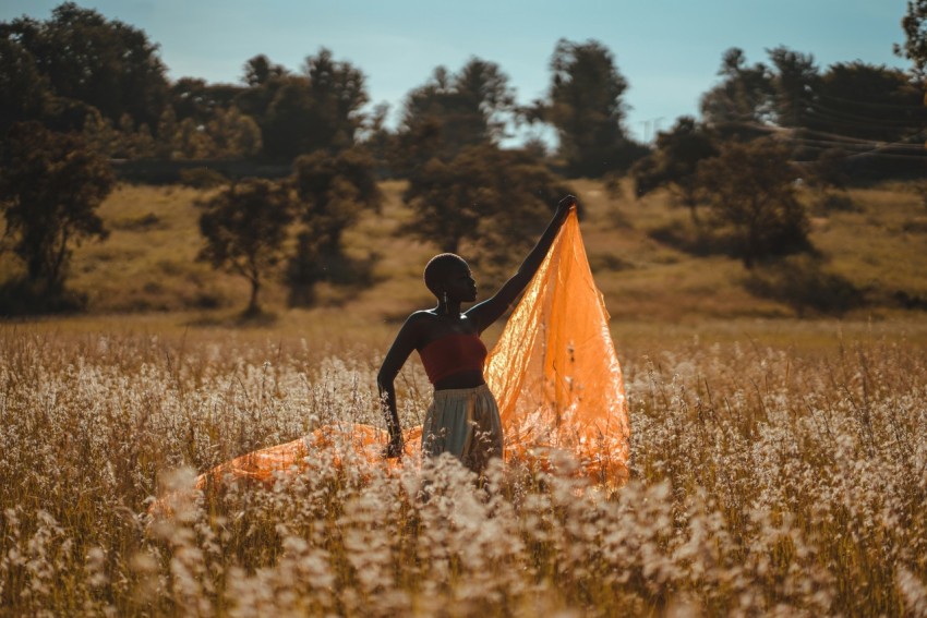 woman standing and holding orange textile at the field during day