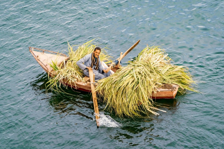 man in white shirt sitting on brown wooden boat on body of water during daytime