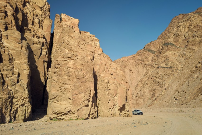 a car driving on a dirt road between large rocky cliffs