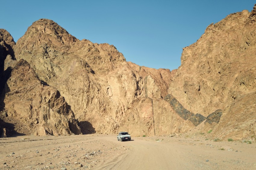 a car driving on a dirt road between large rocky mountains