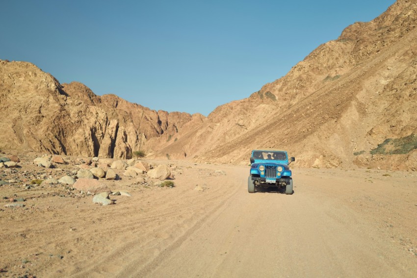 a blue truck driving on a dirt road in the mountains