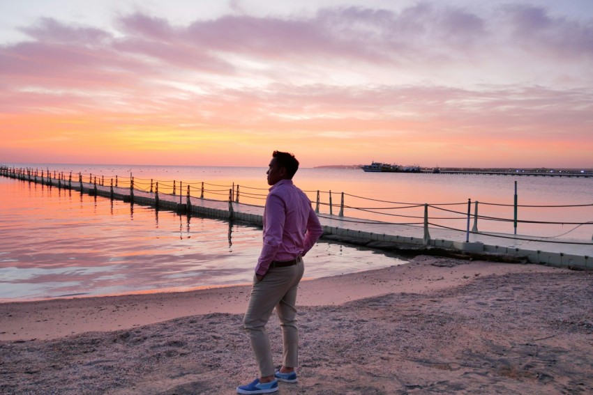 woman in white jacket and blue denim jeans standing on beach during sunset