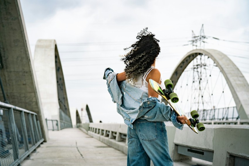 a woman holding a skateboard on a bridge