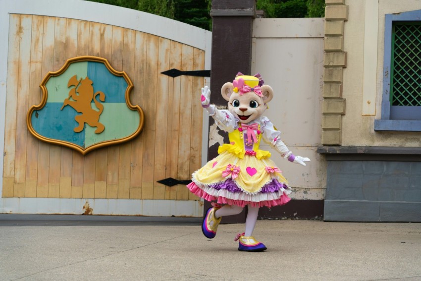 a teddy bear dressed in a dress is dancing in front of a sign 3