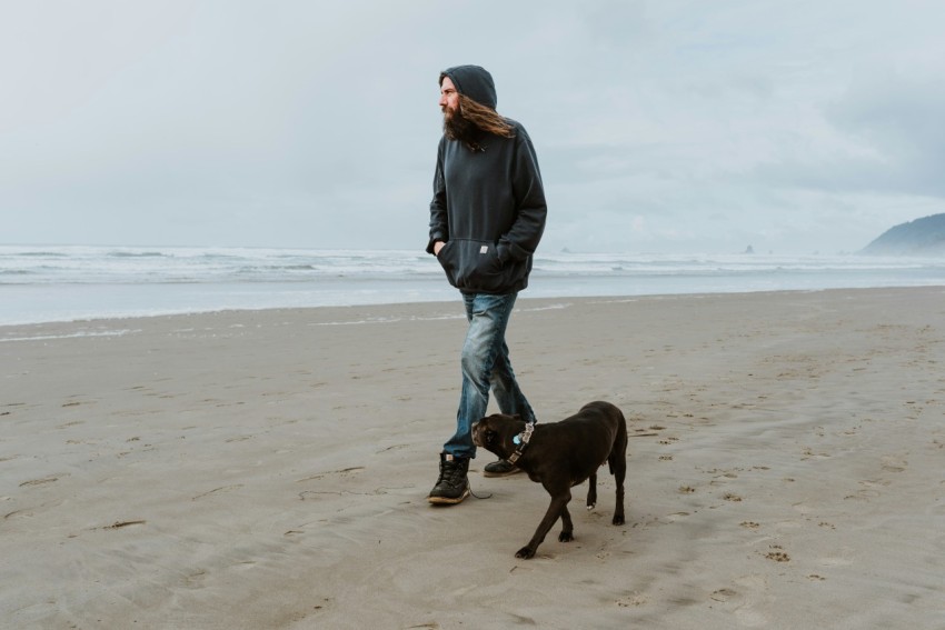 a man walking a dog on a beach hR