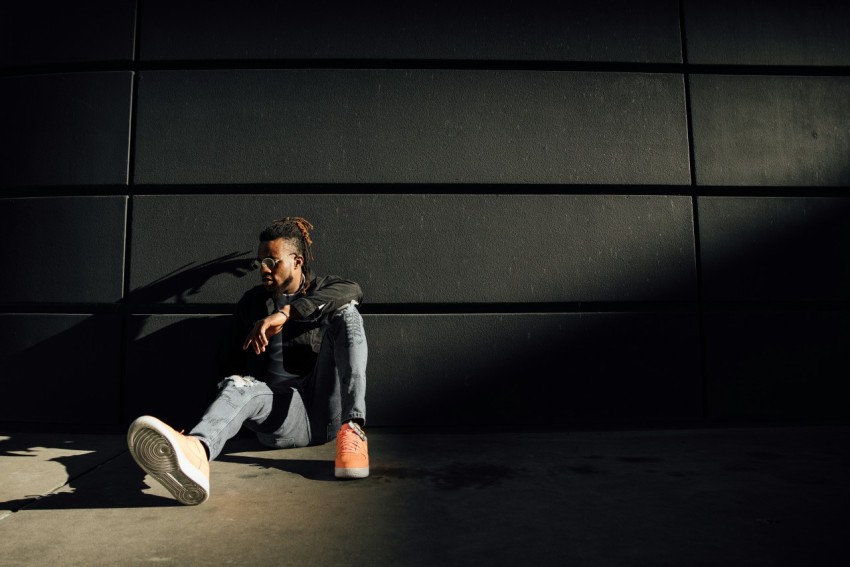 man in black jacket and blue denim jeans sitting on floor