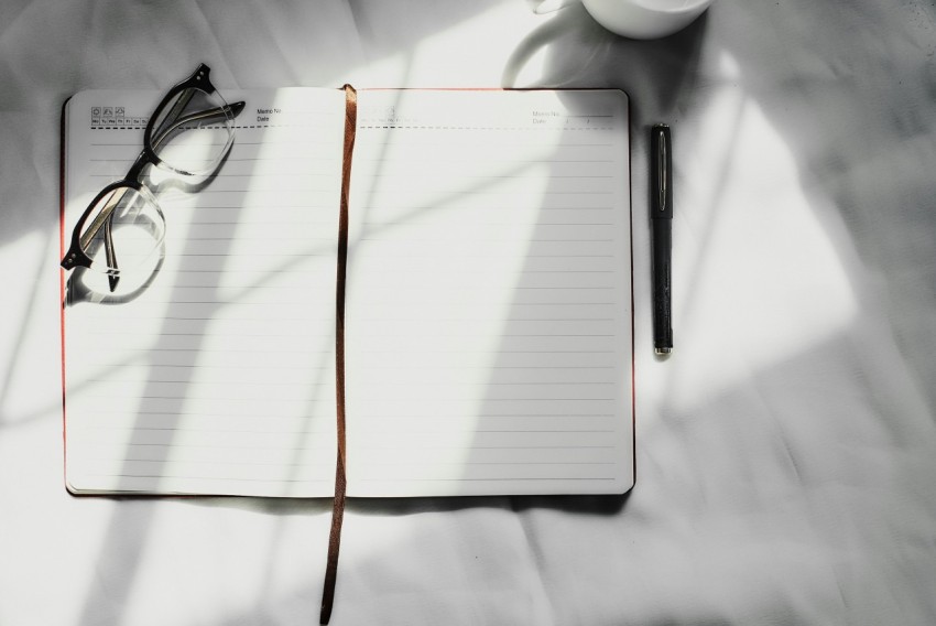 a notebook with a pen glasses and a cup of coffee