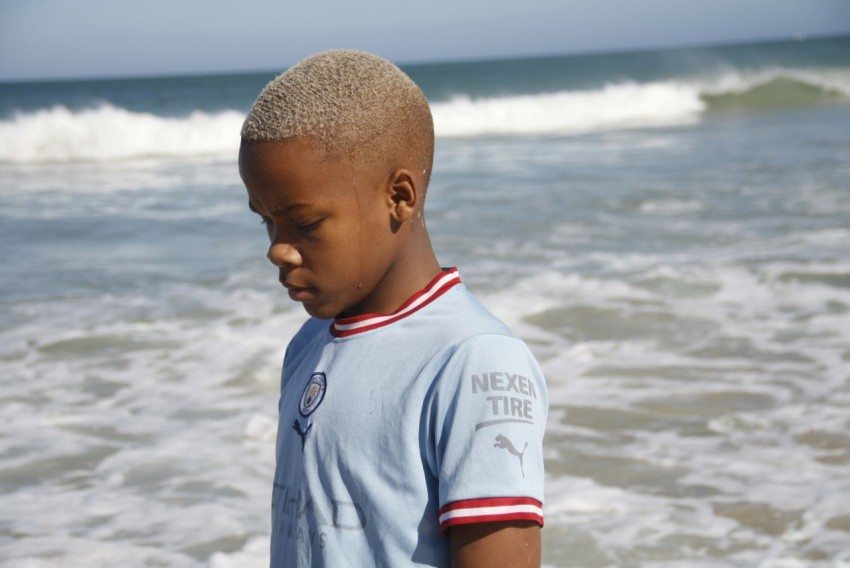 a young boy standing on top of a beach next to the ocean pSEn3z