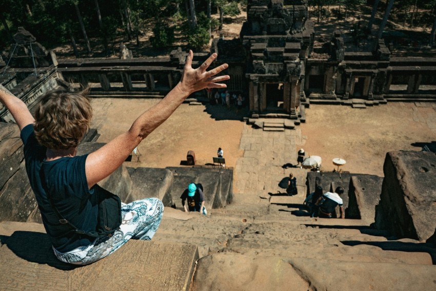 man in black t shirt and blue denim jeans sitting on brown rock formation during daytime