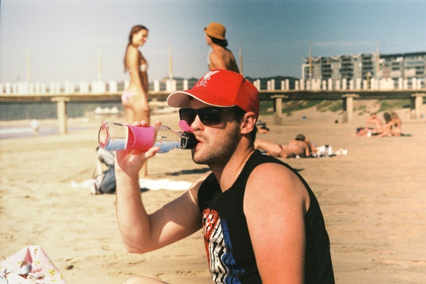 a man sitting on the beach drinking from a pink cup