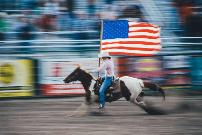 time lapse photo of man carrying us flag while riding brown horse