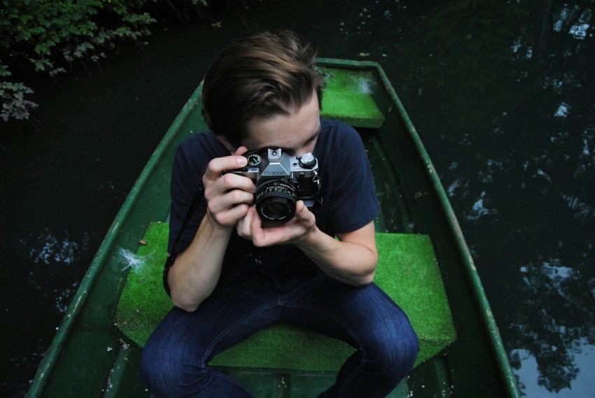 man in black t shirt and blue denim jeans riding on row boat holding bridge camera on focus photo