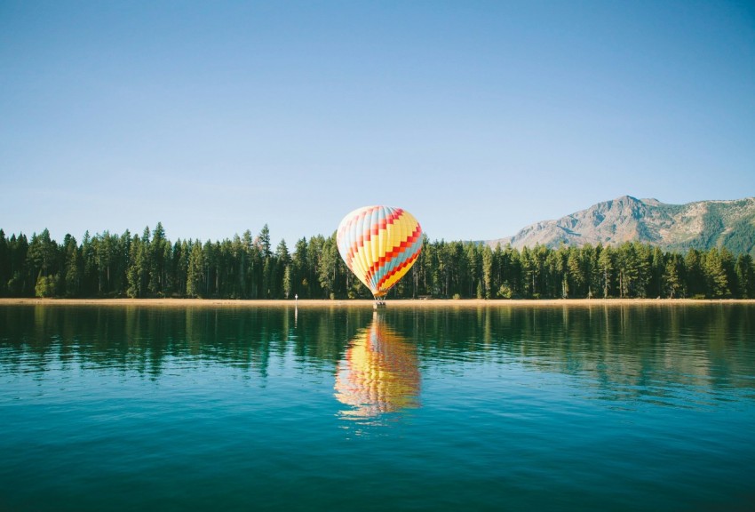 yellow red and blue hot air balloon near trees and body of water under blue sky during daytime