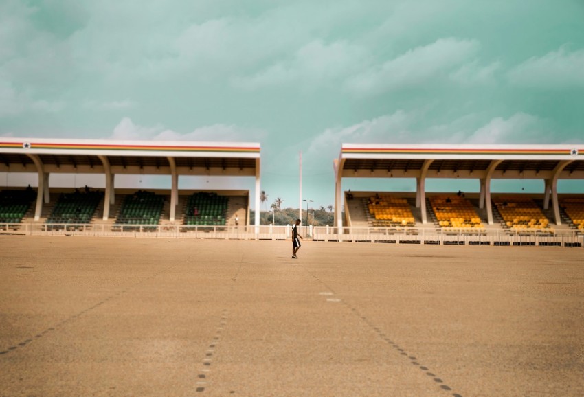 a man walking across a parking lot next to a stadium H