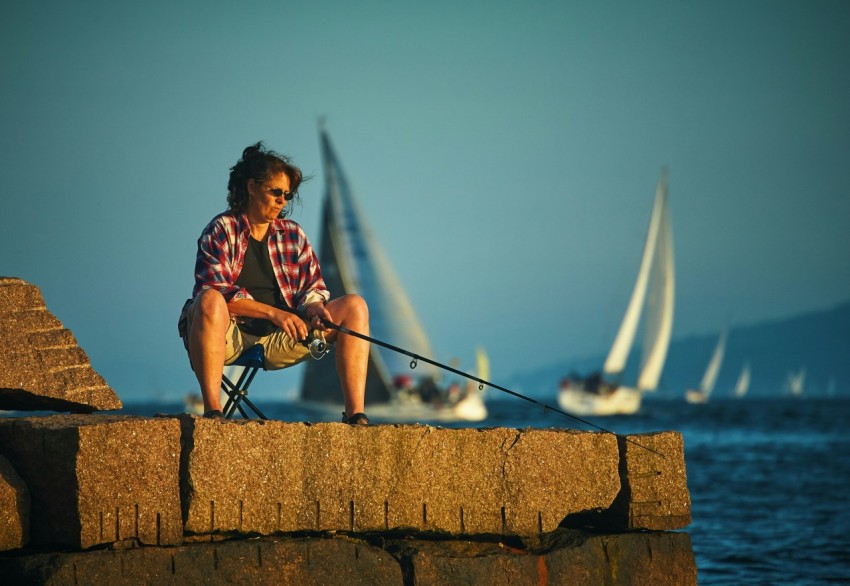 woman sitting down holding black fishing rod waiting for fish