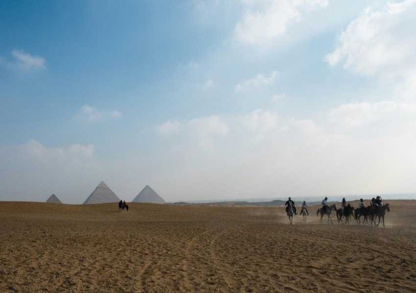 a group of people riding camels in front of pyramids