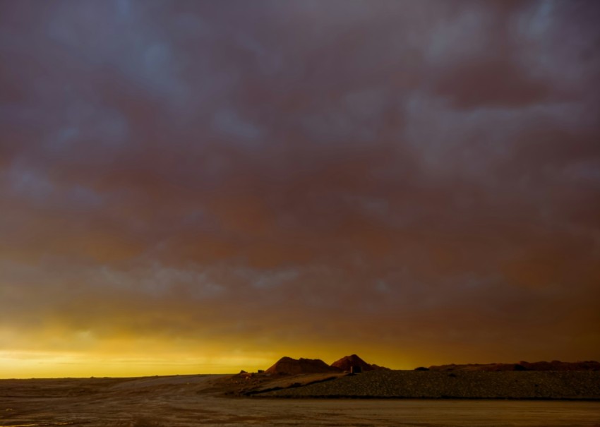 a cloudy sky over a desert with a mountain in the distance