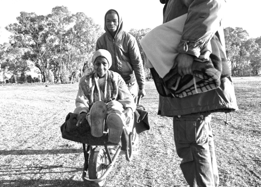 grayscale photo of man pushing wheelbarrow with riding woman