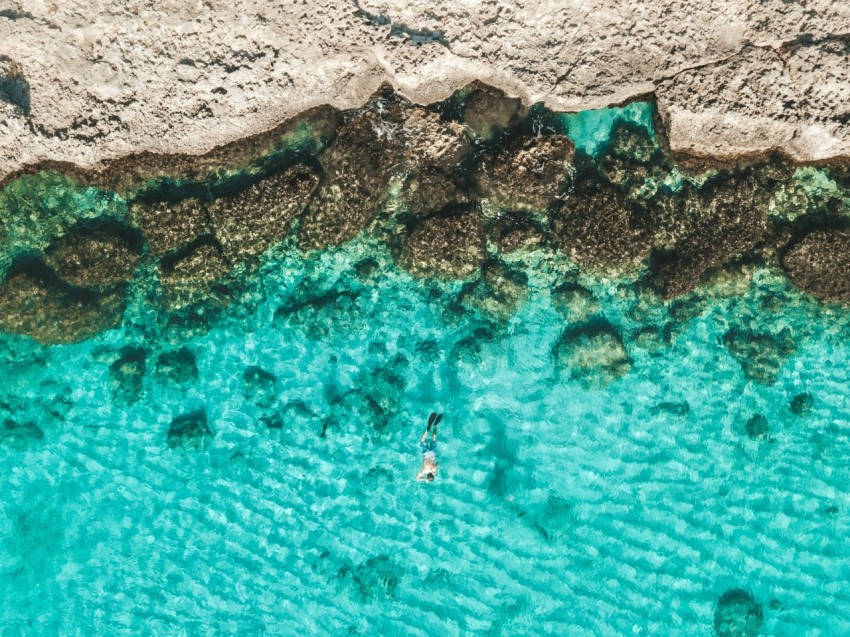 person in blue water near brown rock formation during daytime