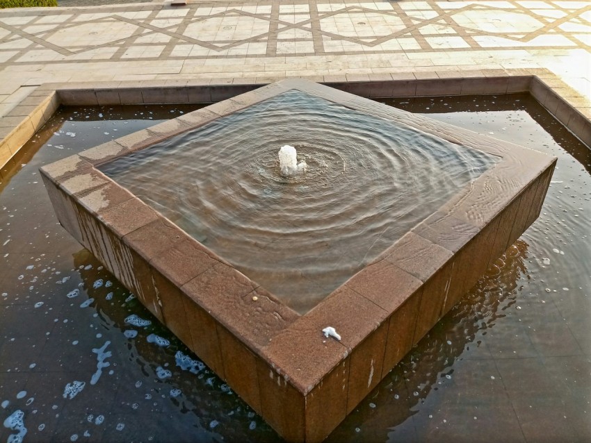 a square fountain with a white bird in it