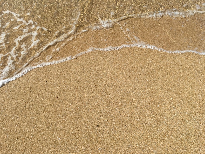 a sandy beach with a wave coming in to shore