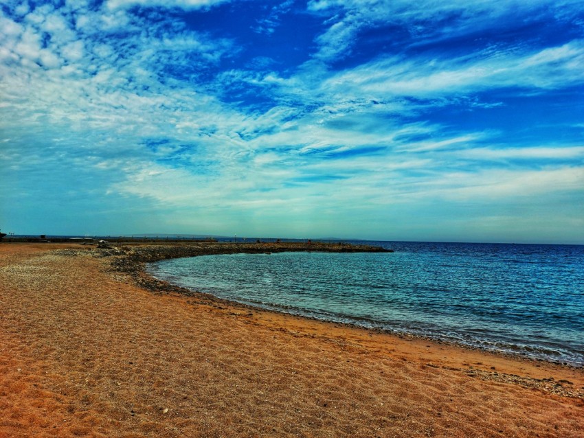 a sandy beach next to the ocean under a blue sky