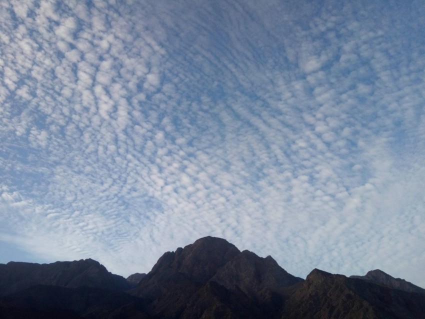 a group of mountains under a cloudy blue sky