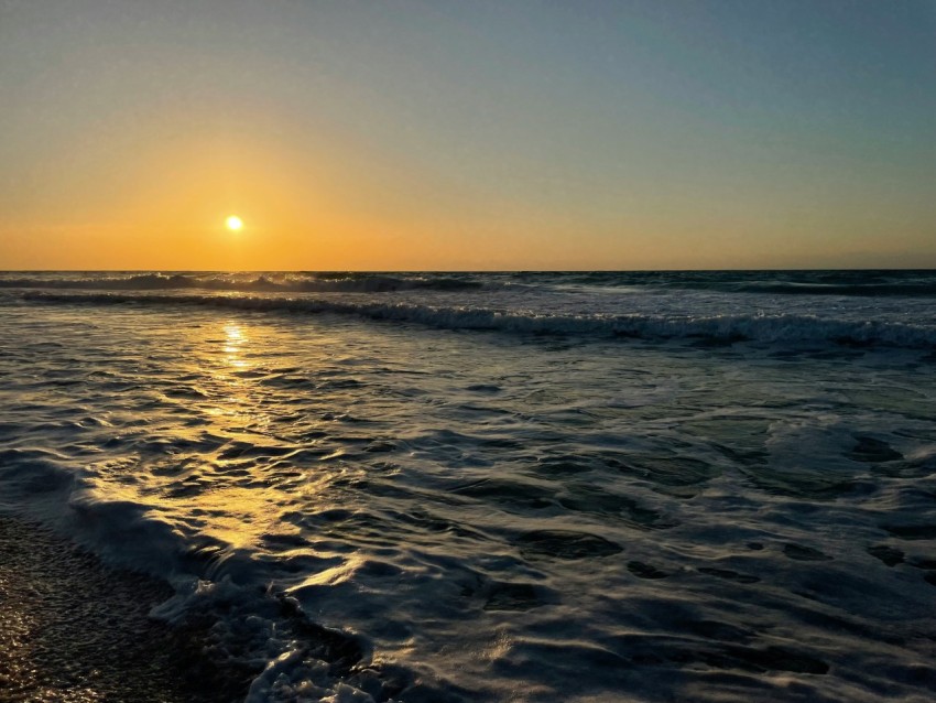 a body of water with waves and the sun setting