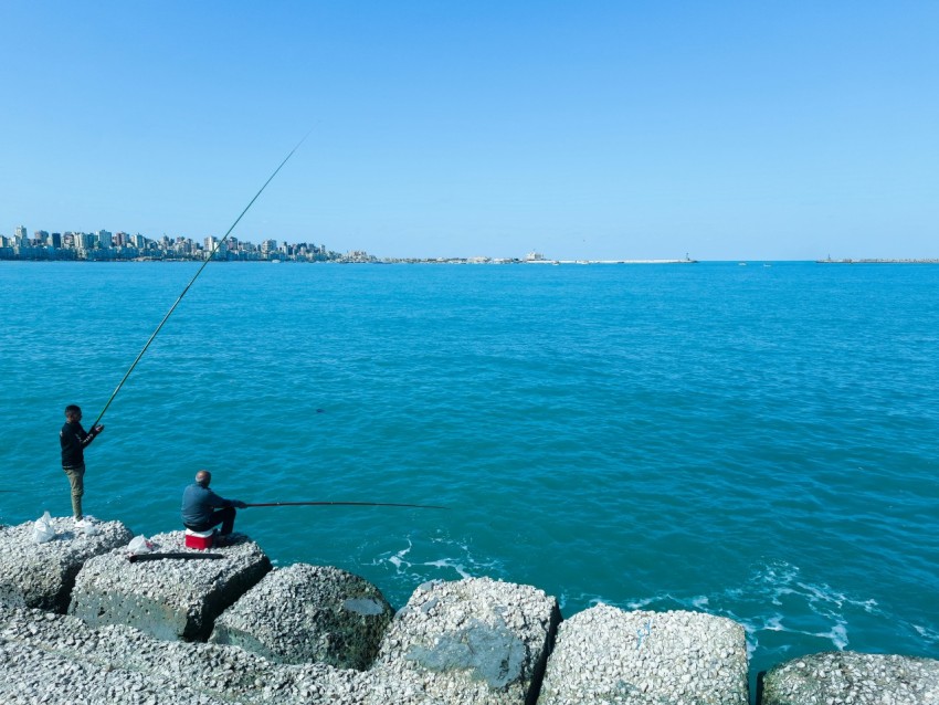 a man sitting on a rock next to a body of water