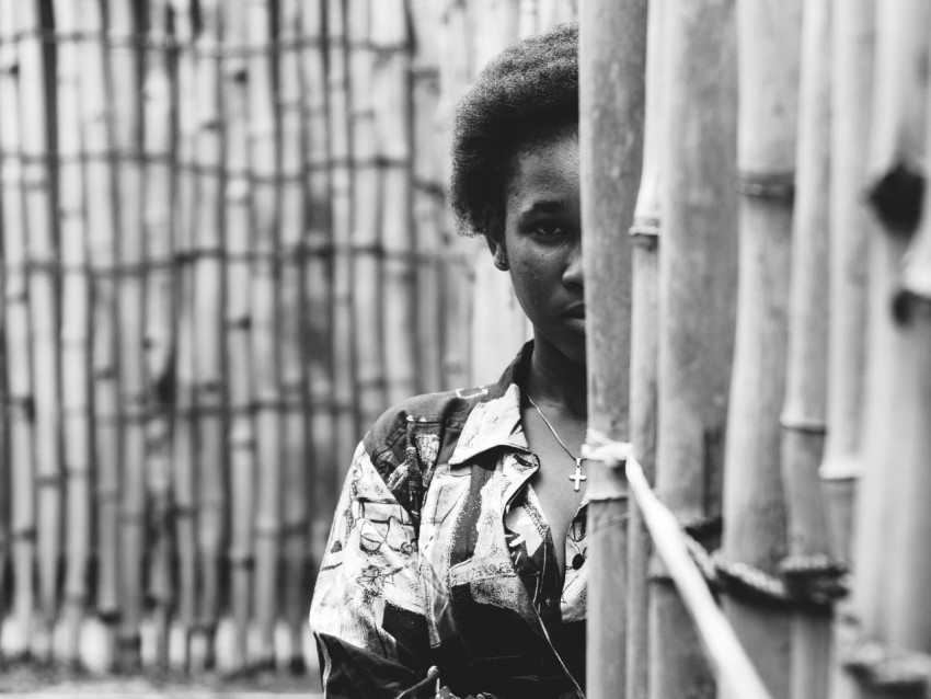 grayscale photo of person hiding on bamboo wall