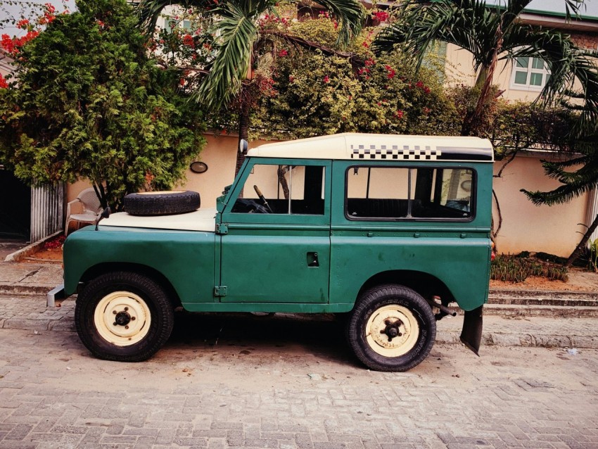 green and white off road vehicle parked outside wall near trees