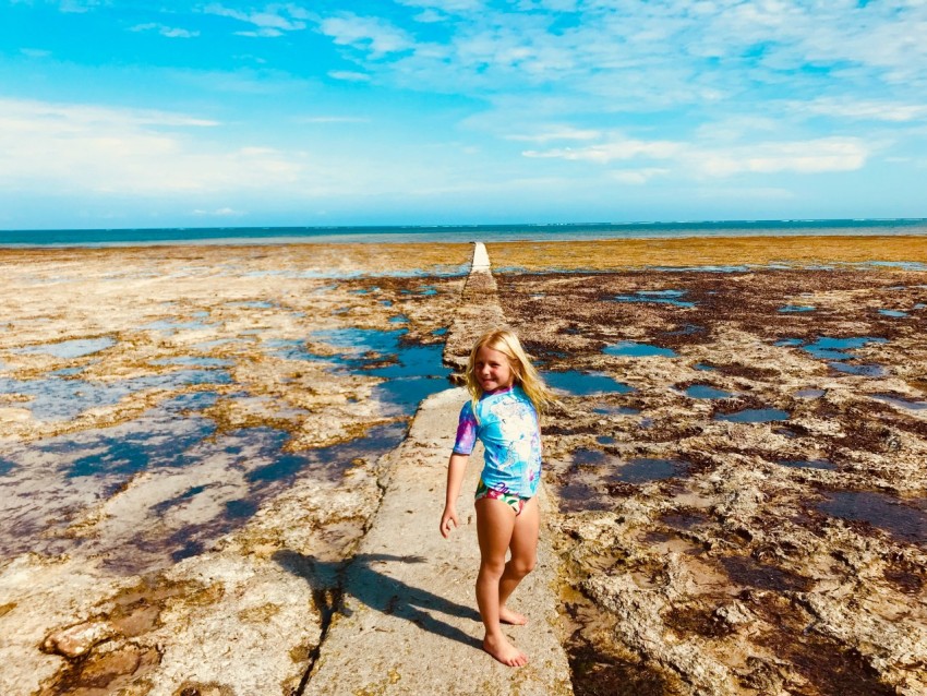 girl in blue and white bikini standing on rocky shore during daytime