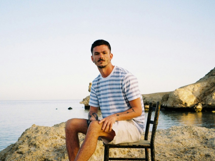 man in white and blue striped polo shirt sitting on brown wooden bench near body of during