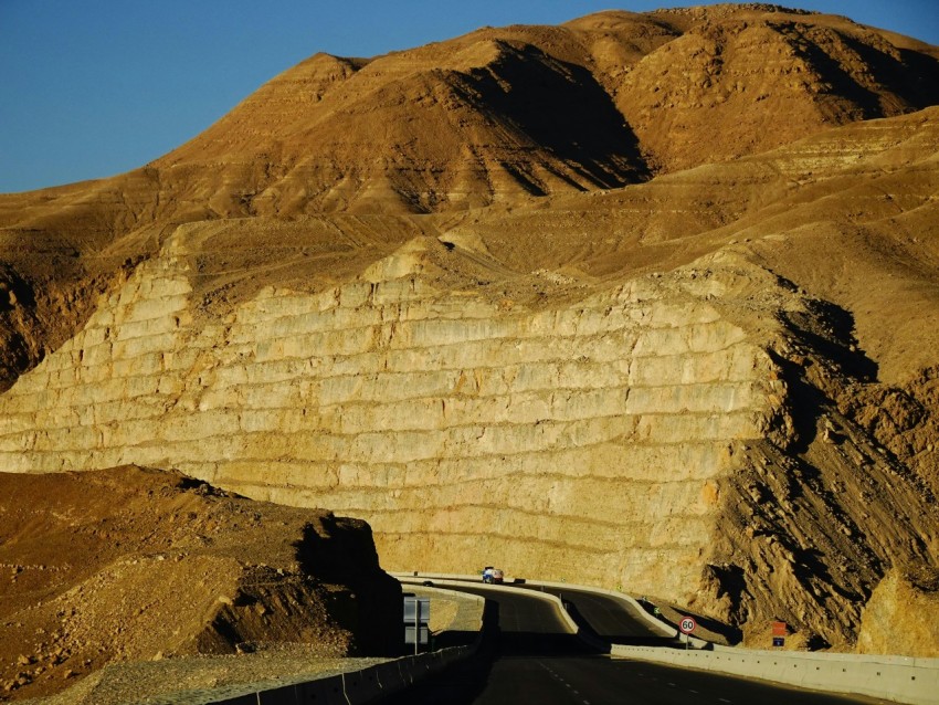 a car driving on a road in front of a large rock cliff