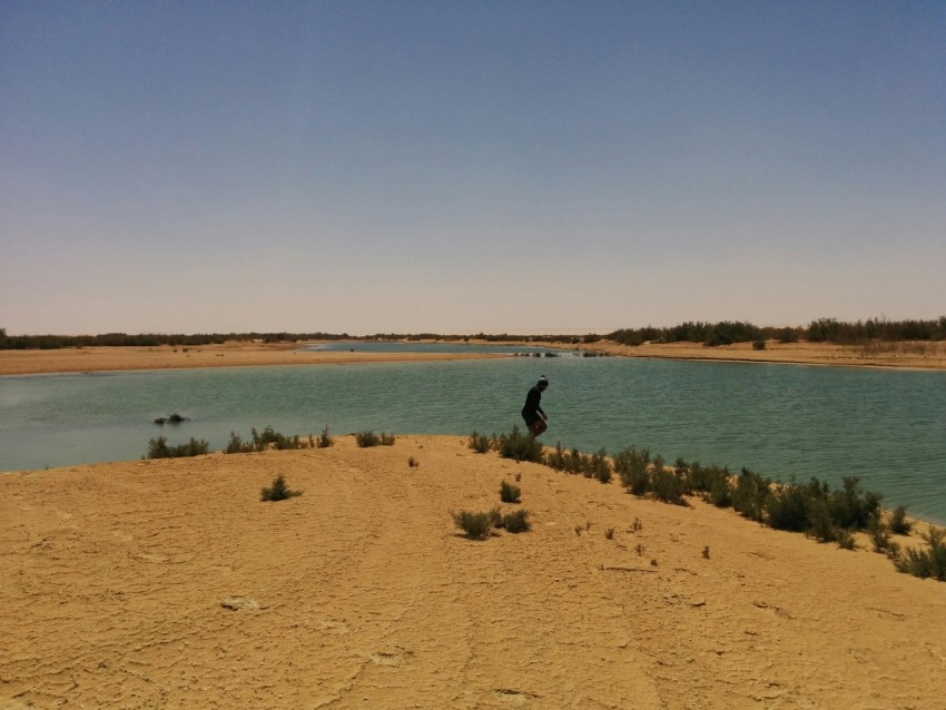 a man standing on top of a sandy hill next to a lake vsL