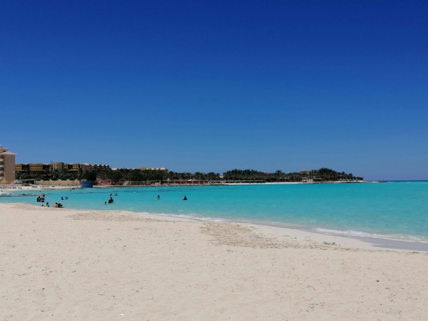 a sandy beach with blue water and people on it 5d3Pn9r