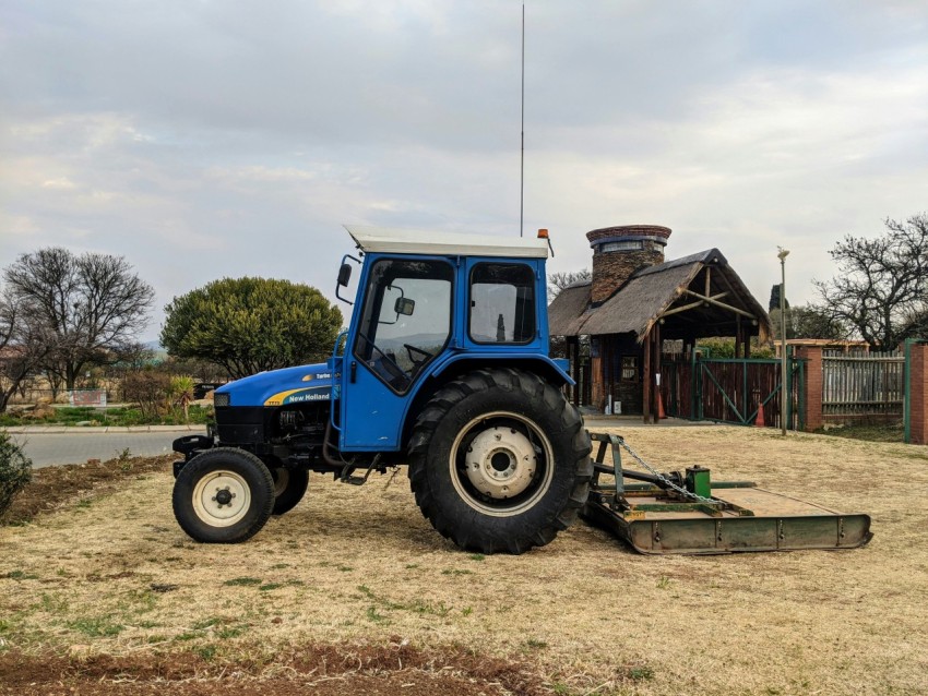 blue tractor on green grass field near brown wooden house under white clouds during daytime