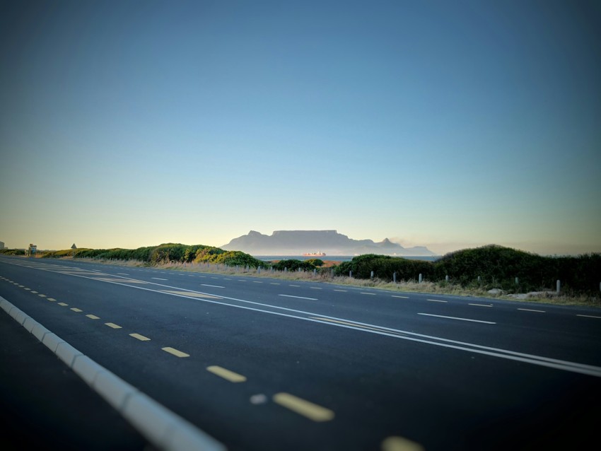 grey asphalt road beside mountain under blue sky