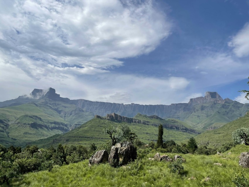 green grass field and green mountains under blue sky and white clouds during daytime