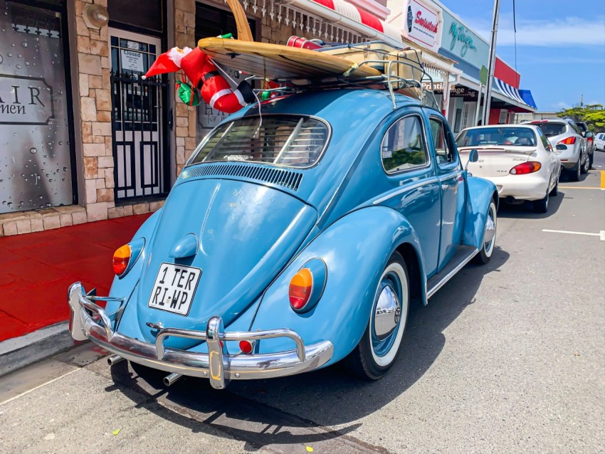 blue volkswagen beetle parked beside brown wooden post during daytime