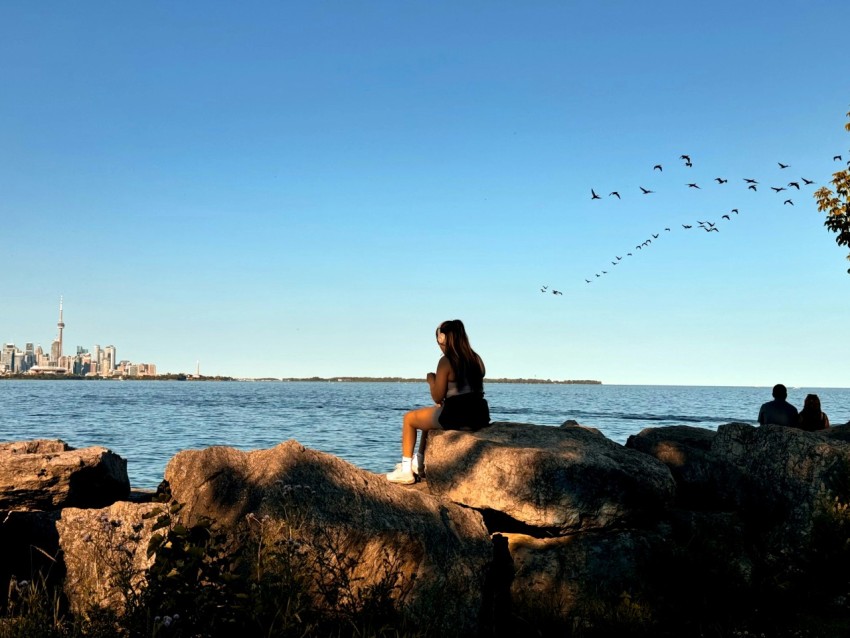 a woman sitting on top of a rock next to a body of water