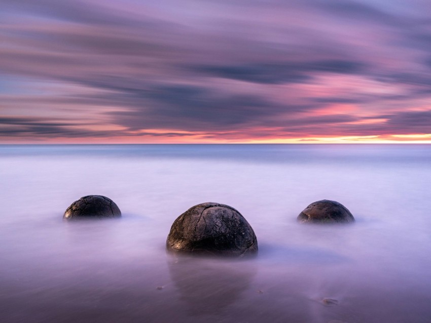 black rock on body of water during sunset