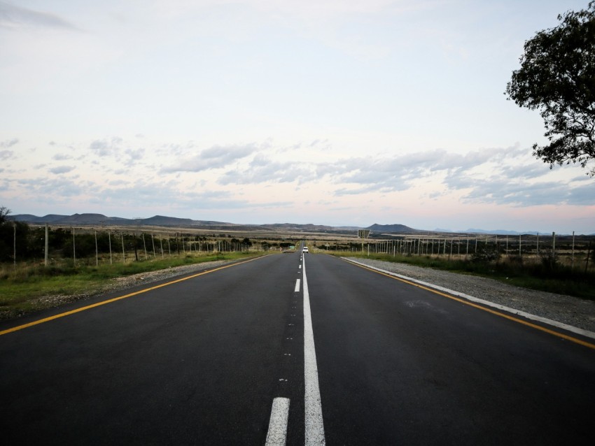 an empty road with a fence and a field in the background