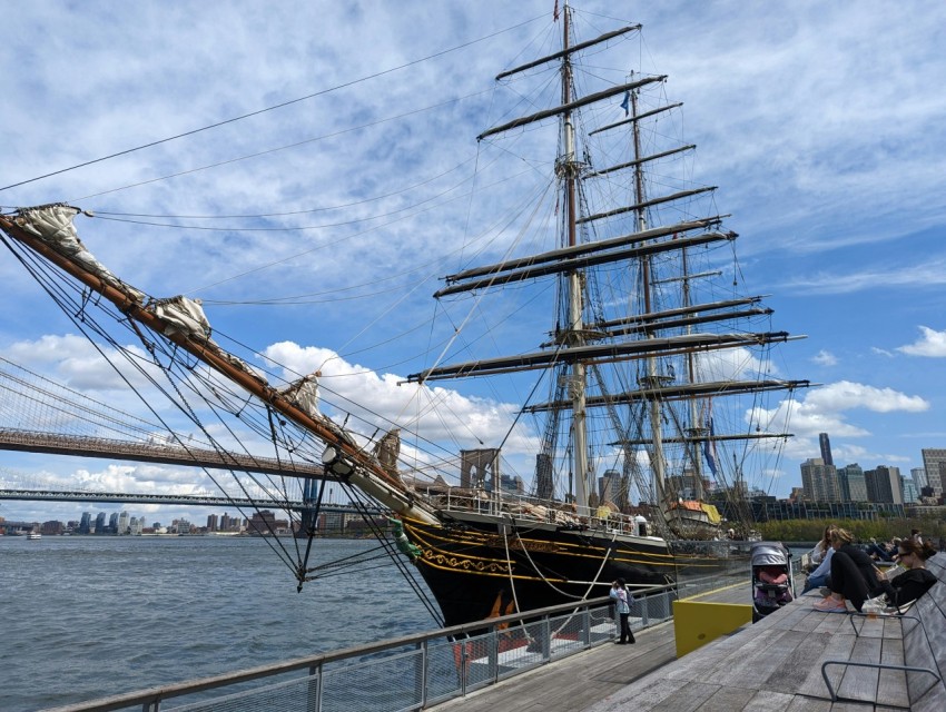 a tall ship docked at a pier with people walking on it