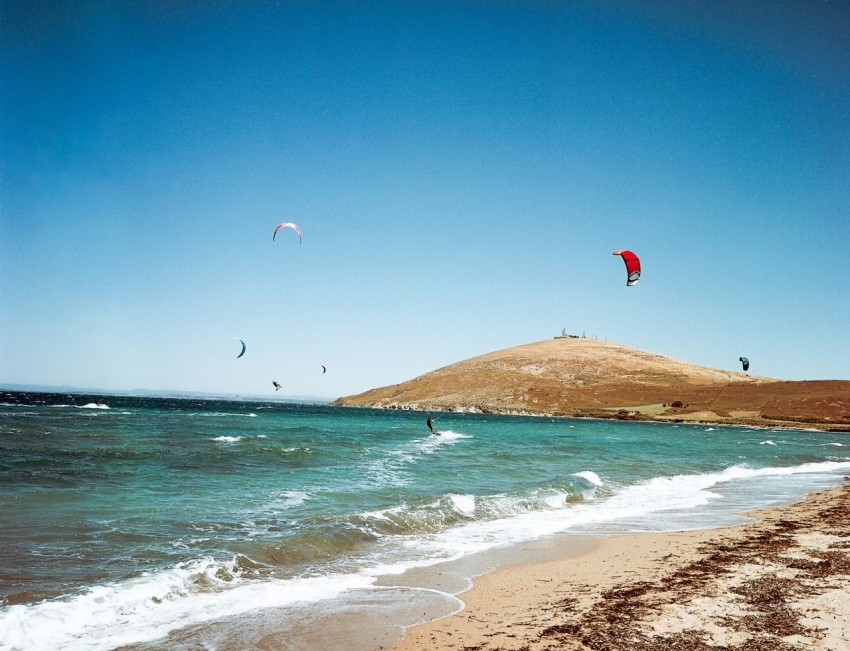 a group of people flying kites on top of a sandy beach