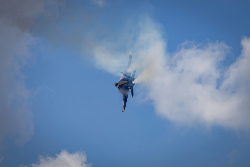 a fighter jet flying through a cloudy blue sky