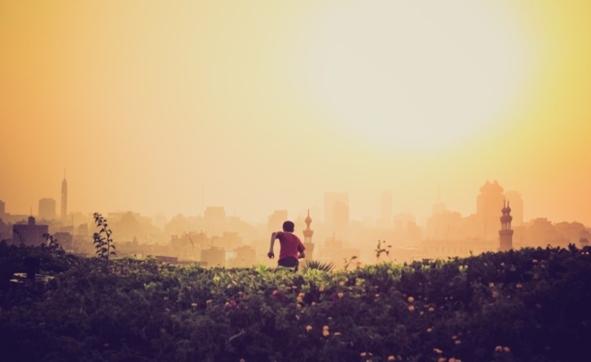 man running towards the city on green grass field during golden time J8k