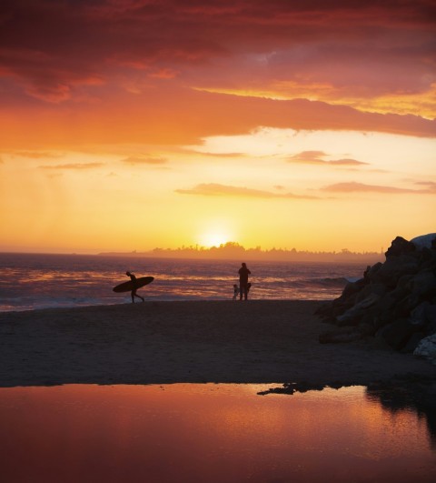 silhouette of 2 people standing on rock formation near sea during sunset