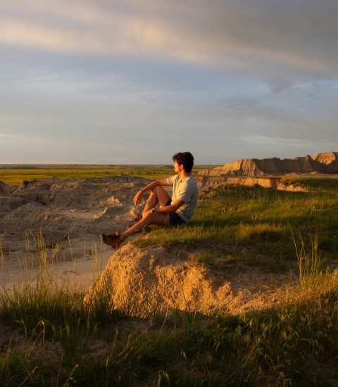 a man sitting on top of a rock next to a body of water