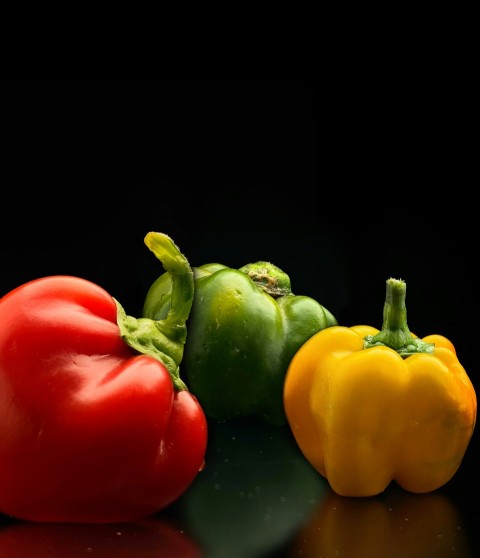 three different colored peppers on a black surface